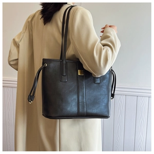 Close-up of black leather tote bag with gold metal plaque and stylish drawstring details