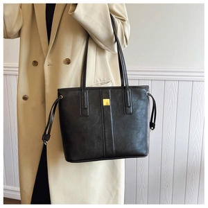 Close-up of black tote bag with gold metal buckle and drawstring on a beige coat