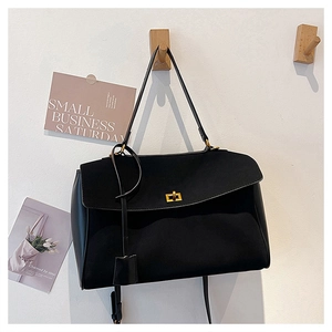 Close-up of black suede tote bag with a golden twist lock on a minimalist wall