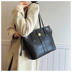 Detail of a black minimalist tote bag with a gold metal plate on light khaki coat