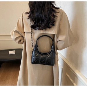 Détail d'un sac à main en cuir matelassé noir avec bandoulière et trench-coat beige