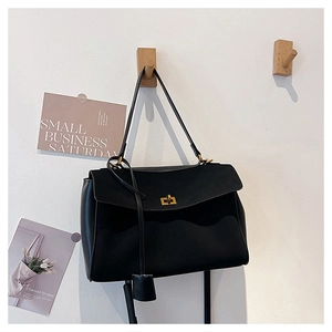 Detail of matte black suede tote bag hanging on wooden hook with golden hardware