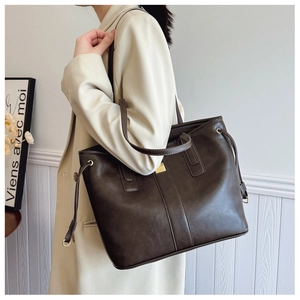 Detail of large dark brown leather tote bag with gold metal plaque and side drawstrings