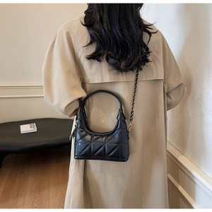 Vue arrière d'un sac matelassé noir avec chaîne porté sur un trench-coat moderne beige