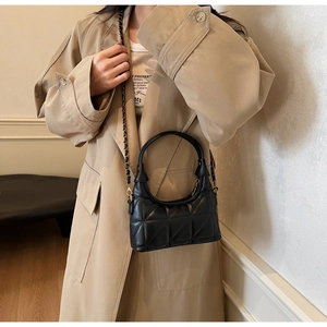 Détail d'un sac à main matelassé noir avec chaîne dorée porté sur un trench-coat