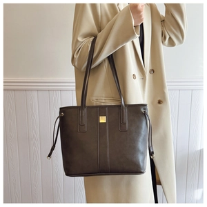 Detail of dark brown faux leather tote bag with gold metal hardware and drawstring sides