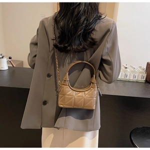 Détail d'un sac à bandoulière matelassé chameau foncé avec chaîne dorée sur un mannequin