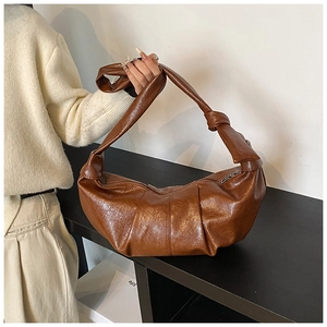 Close-up of brown pleated leather croissant bag with knotted shoulder strap detail