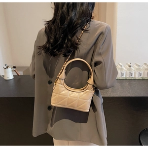 Détail du sac hobo matelassé beige avec chaîne dorée porté par un mannequin