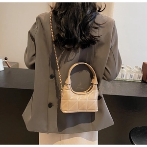 Détail du mannequin portant un sac bandoulière beige matelassé avec une chaîne dorée
