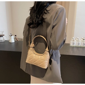 Détail d'un sac matelassé beige avec poignée ronde et bandoulière chaîne sur modèle