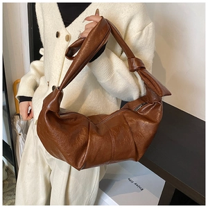 Close-up of brown pleated crescent shoulder bag with retro leather texture and knot detail