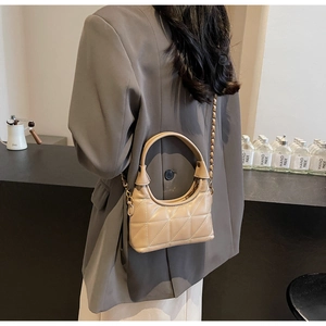 Sac bandoulière matelassé beige avec chaîne porté avec un blazer gris de style moderne