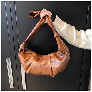 Detail of a brown pleated crescent bag with a unique knotted shoulder strap and glossy finish