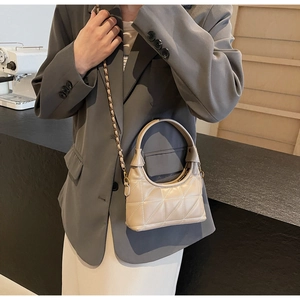 Détail d'un sac à main beige matelassé avec bandoulière chaîne dorée dans un café moderne