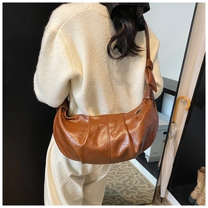 Detail of a brown pleated croissant bag with soft texture and knotted strap on model