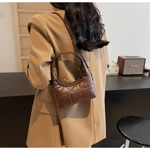 Détail du sac matelassé en cuir marron foncé avec bandoulière chaîne sur costume kaki