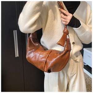 Close-up of brown soft leather dumpling bag featuring pleated texture and knot detail