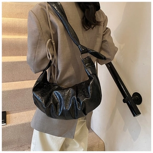 Side view of a black soft leather crescent hobo bag with pleated texture on a model