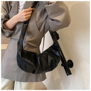 Detail of black glossy pleated dumpling bag featuring vintage oil wax leather texture