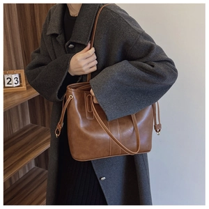 Brown leather tote bag shoulder carry view showing large capacity on grey coat