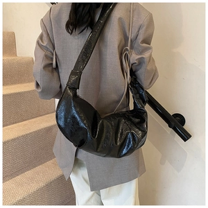 Glossy black crescent moon dumpling bag with soft pleated texture and wide shoulder strap