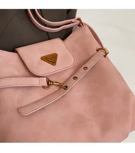 Detail of pink faux suede shoulder bag with golden triangle logo and brass hardware