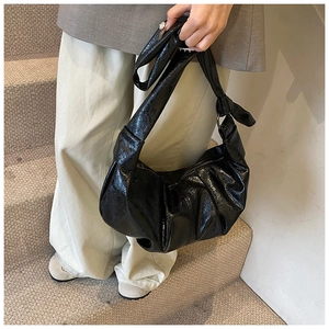 Detail of glossy pleated leather dumpling bag with decorative knot and zipper