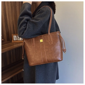 Close-up of brown faux leather tote bag with gold buckle and side drawstring detail