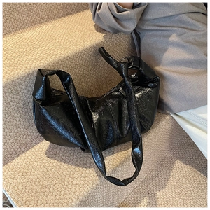 Detail of glossy black dumpling bag with knotted shoulder strap and silver ring accents