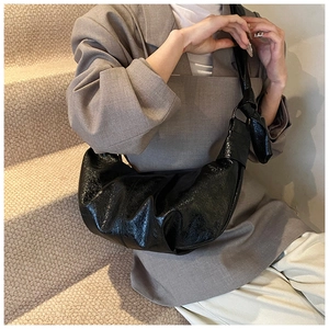 Detail of black glossy croissant bag with knotted shoulder strap worn with a grey suit