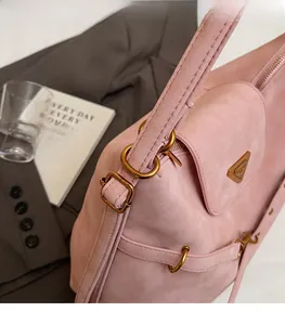 Pink suede shoulder bag featuring an adjustable strap and metal triangular logo plate