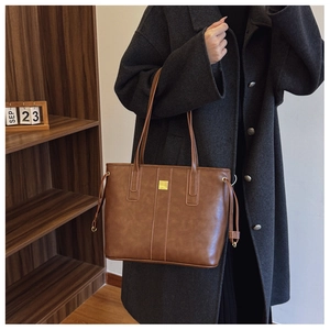 Detail of dark brown faux leather tote bag with gold hardware and side drawstring details