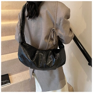 Detailed view of black glossy pleated half-moon bag on shoulder against minimalist stairs
