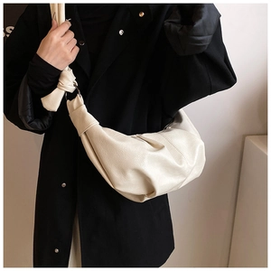 Detail of soft off-white crescent bag featuring knot shoulder strap and metal ring