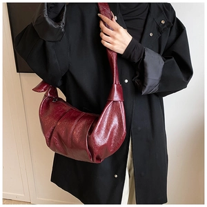 Detail of burgundy leather croissant bag with soft pleated texture and integrated wide strap