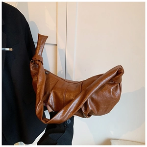 Detailed shot of brown pleated croissant bag with knotted strap and oil-wax leather texture