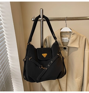 Detail of a black nylon tote bag featuring a gold triangle logo and metallic buckle strap