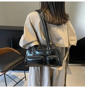 Detail of glossy black shoulder bag featuring dual front zip pockets and silver hardware