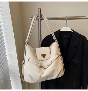 Detail of matte cream tote bag showing triangle metal logo and minimalist hardware accents