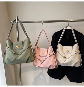 Detailed view of suede tote bags in green, beige and pink with metal triangle emblem