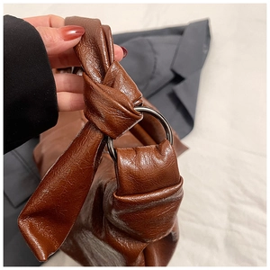 Detail of a brown leather dumpling bag showing knotted strap and silver metal ring connector