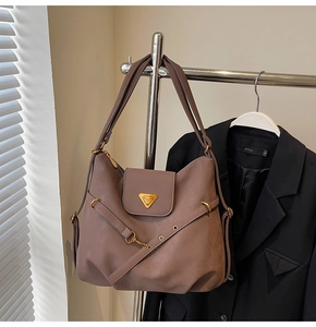 Close-up of vintage brown shoulder bag showing golden triangular plaque and leather texture