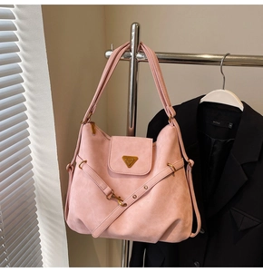 Close-up of pink suede tote bag featuring a gold triangle logo and textured strap details