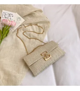 Detail of cream woven envelope bag featuring gold chain and H-shaped metal lock