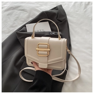 Détail du sac à main en cuir crème élégant avec boucle dorée sur fond de costume