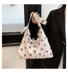 Dettaglio della borsa tote in tela bianca con stampe di fragole e un fiocco sulla tracolla
