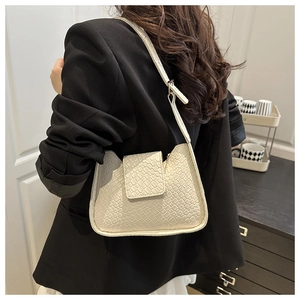 Gros plan du sac à bandoulière tressé beige porté avec un blazer noir chic