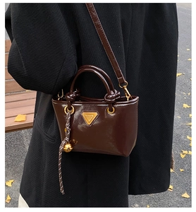 Détail d'un sac à main en cuir marron foncé avec plaque triangulaire dorée et poignée nouée
