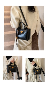 Détail d'un sac cabas noir brillant avec logo en métal doré et breloque cloche tressée